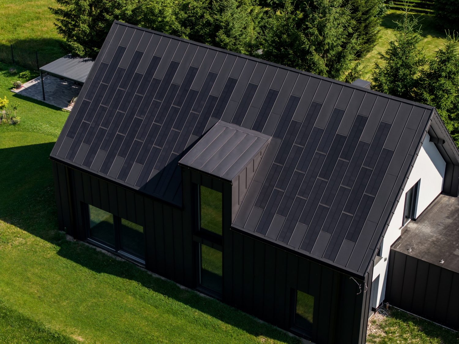 Dark modern house with a SolRoof FIT VOLT standing-seam solar roof, aerial view; manufacturer photo of a European installation