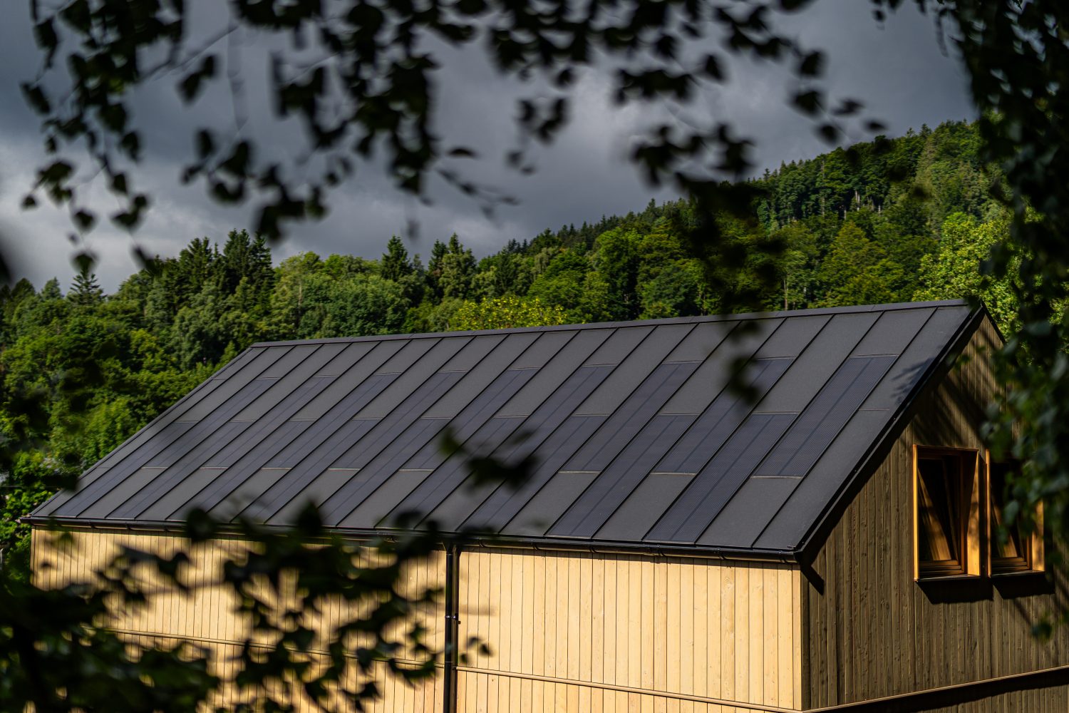Timber cabin among trees with a dark SolRoof FIT VOLT standing-seam solar roof; manufacturer photo of a European installation