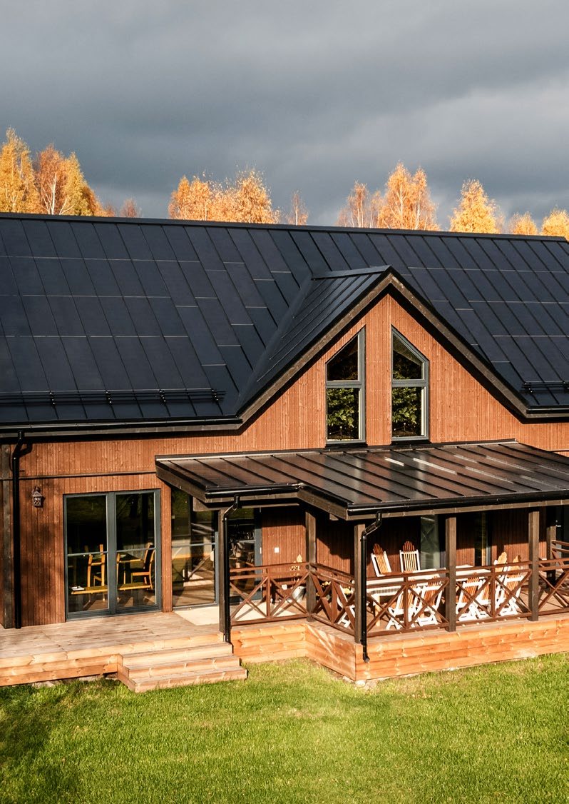 Timber house with a covered porch and a dark Roofit Velario standing-seam solar roof; manufacturer photo
