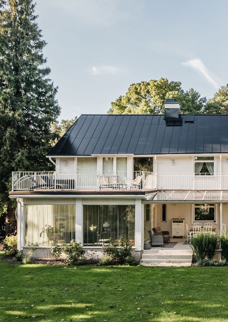 White two-story house with a balcony and a dark Roofit Velario standing-seam solar roof; manufacturer photo