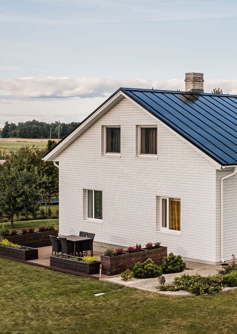 White two-story house with a blue-gray Roofit Velario standing-seam solar roof; manufacturer photo
