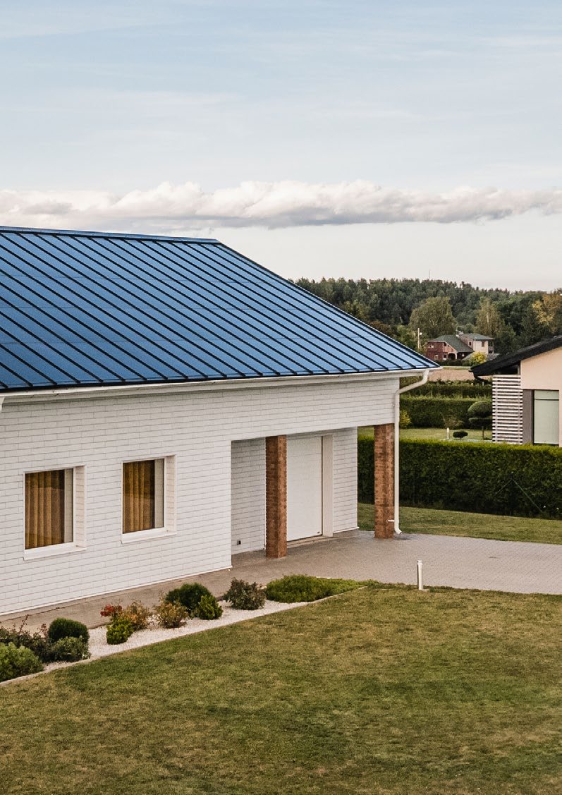 White house and attached garage under a blue-gray Roofit Velario standing-seam solar roof; manufacturer photo